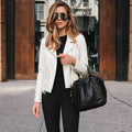 Woman in a white jacket and black pants holding a black handbag on a city street.
