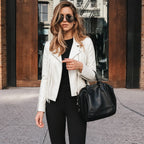 Woman in a white jacket and black pants holding a black handbag on a city street.