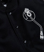 Zoom  catalog layout of the Leveljacket Def Jam Recordings black varsity jacket, displaying a premium black wool body with black leather sleeves, custom white embroidered turntable needle art on the front chest, and a bold white Def Jam Recordings typography patch layout across the back.