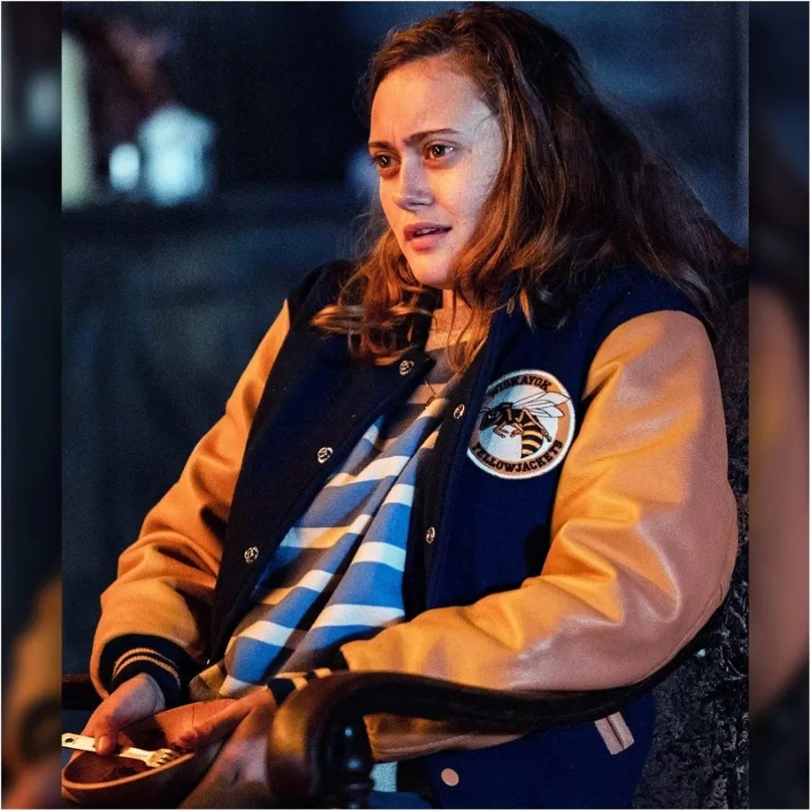 Person wearing a letterman jacket with a logo, sitting indoors.