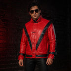 A man wearing a bright red leather jacket with bold black contrast panels and black pants, standing against a dark brick wall.
