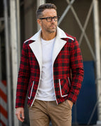 A man wearing a red and black plaid blazer with a white collar and white piping details, layered over a white t-shirt and khaki pants.